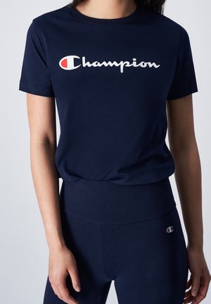 T-shirt Champion bleu marine avec logo sur la poitrine et leggings bleu marine assortis avec petit logo Champion sur la hanche, porté par une personne.