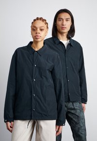 Vestes légères et foncées avec fermetures à bouton et poignets élastiques, présentant une coupe décontractée et des cordons de serrage ajustables à l'ourlet.