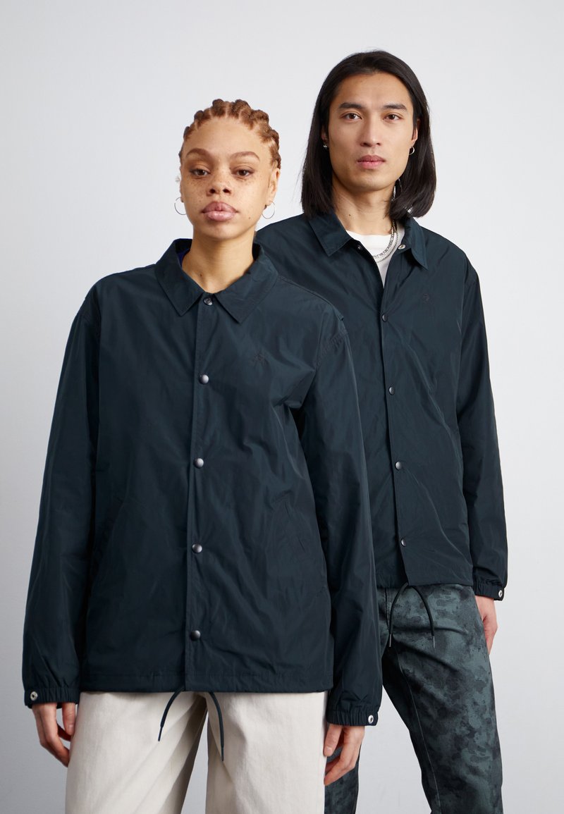Vestes légères et foncées avec fermetures à bouton et poignets élastiques, présentant une coupe décontractée et des cordons de serrage ajustables à l'ourlet.