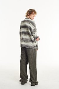 Textūruotas, dryžuotas megztinis pilkai žaliais atspalviais, derinamas su laisvais tamsiai pilkais kelniais. Apranga pasižymi laisvu siluetu ir minkšta medžiaga.