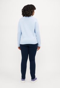 Lyseblå genser, slanke sjøgrønne bukser og lilla sneakers. Genseren har lange ermer, rund hals og ribbestrikket kant. Slank passform er synlig.