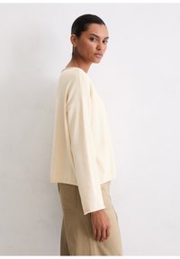 Cremefarbener, weicher Stoffpullover mit lockerer Passform, rundem Halsausschnitt und langen Ärmeln. Kombiniert mit hellen Khaki-Hosen. Einfaches und minimales Design.