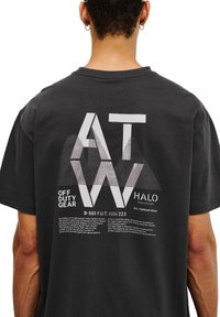 Svart bomullströja med en stor vit grafik med vinklade bokstäver, textdetaljer och en texturerad yta på baksidan.