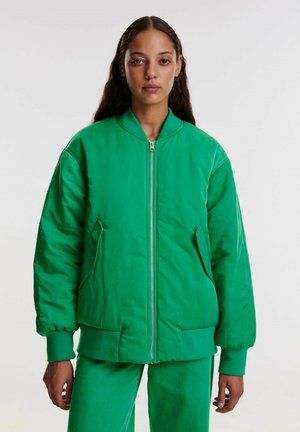 Groene bomberjack van gladde stof, met een voorrits, geribbelde mouwen en twee zijzakken. Gekoeld met bijpassende groene broeken.