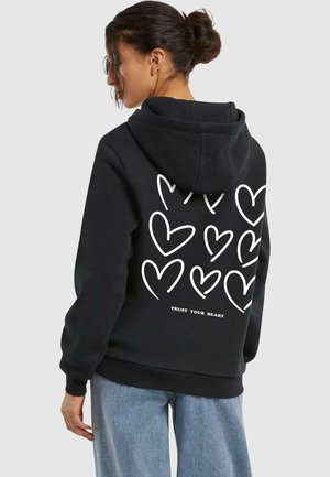 Felpa nera con cappuccio e tasca frontale, caratterizzata da contorni bianchi a forma di cuore e dalla scritta "FIDATI DEL TUO CUORE" sul retro. Realizzata in tessuto morbido.