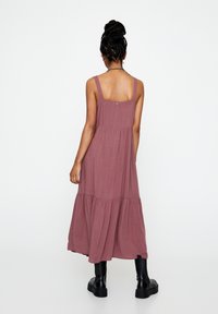 Vestido maxi sin mangas de rosa empolvado con tirantes ajustables, diseño en capas, hecho de tela ligera. Llevado con botas de plataforma negras.