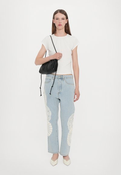 Maglietta bianca a maniche corte, jeans azzurri chiari con dettaglio in pizzo bianco sui lati, borsa nera e ballerine bianche con punta. Taglio e design semplici.