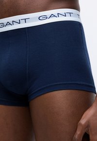 Ingrandimento di una persona che indossa boxer blu navy GANT con elastico bianco recante il logo del marchio.