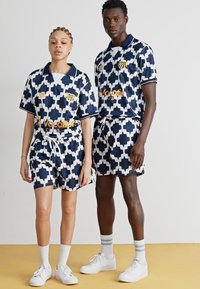 Marinblå och vit mönstrad matchande sportkläder, som består av en t-shirt med kort ärm och shorts. Inkluderar shorts med dragsko och logotyp på bröstet.