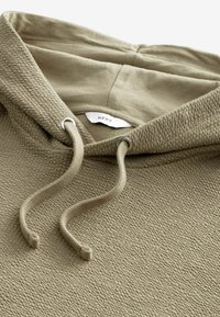 Khakifarbene Kapuzenjacke aus strukturiertem Stoff, mit verstellbaren Kordeln und glattem Innenfutter. Das Etikett trägt die Aufschrift "NEXT". Sie verfügt über ein gemütliches, lässiges Design.