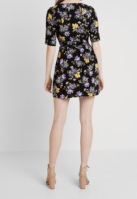 Blumenkleid mit schwarzem Hintergrund, kurzen Ärmeln und Taillengürtel. Akzente in Gelb und Lila schaffen ein lebhaftes Muster.