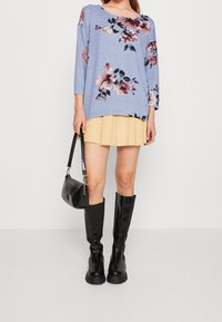 Ljust blå blommig tröja med trekvartslång ärm, tillsammans med en veckad gul kjol. Svarta knähöga stövlar och en liten svart väska fulländar looken.