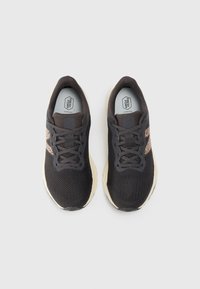 Une paire de chaussures de course en mesh noir avec des semelles beiges et des détails de motif animal sur les côtés, vues d'en haut sur un fond clair.