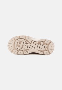 Buffalo sneakersåle i off-white gummi med teksturert grep, med merkevarenlogoen preget i en dekorativ stil i midten.