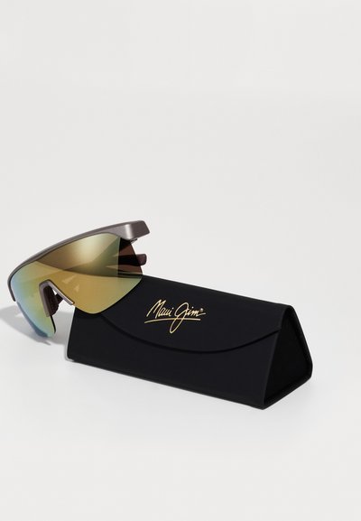 Maui Jim napszemüveg, karcsú szürke kerettel és átmenetes lencsékkel. Fekete háromszögletű tokot tartalmaz, arany logóval díszítve.