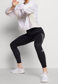 Czarne legginsy z trzema białymi paskami po bokach, zestawione z krótką białą kurtką sportową. Posiadają lekką teksturę i sportowy design.