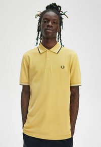 Polo giallo con colletto e chiusura a tre bottoni, con accenti a righe bianche e nere. Logo ricamato sul petto.