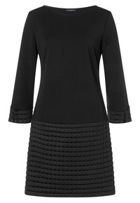 Svart klänning med långa ärmar, som har en slät överdel och en texturerad, vadderad fåll med ett rutmönster. Enkel rund halsringning.