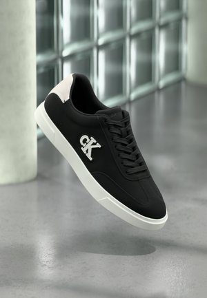 Schwarzer Sneaker mit weißer Sohle, Wildlederakzenten, Schnürsenkeln und gesticktem "CK"-Logo an der Seite. Glatte Textur mit sportlichem Design.
