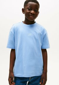Lichtblauwe katoenen t-shirt met korte mouwen, ronde halslijn en een klein grafisch logo op de borst. Gecombineerd met blauwe denim jeans.