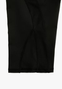 Mustat urheilulegginsit, joissa on sileä ja joustava kangas, sivupaneelien ompelu- ja tiukka muotoilu.