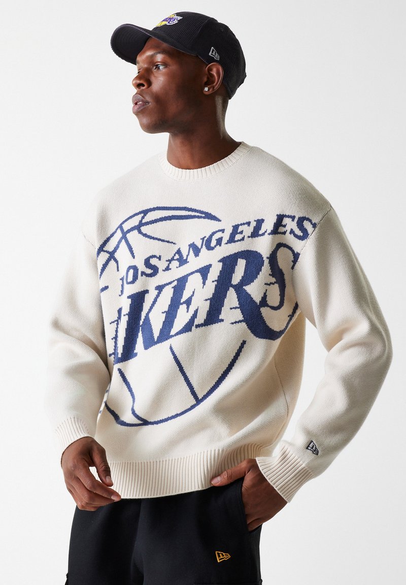 Pulover crem cu un grafic mare al echipei "Los Angeles Lakers" în nuanță de bleumarin. Dispune de un gât rotund, manșete ribbate și tricotat texturat. Purtați-l cu pantaloni scurți închisi la culoare.