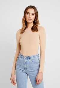 Pika pika tooni nude bodysuit, mis on valmistatud pehmest ja venivast kangast, koos kõrge vöökohaga helesiniste denim pükstega, millel on klassikaline viie taskuga disain.