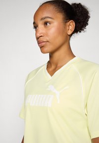 Svijetložuti sportski dres s v-izrezom, kratkim rukavima i bijelim detaljima. Na prednjoj strani ističe se Puma logo.