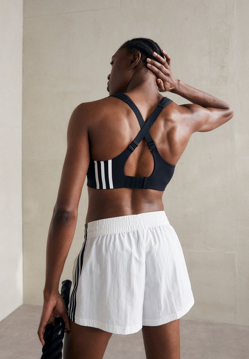 Svart sports BH med kryssrygg og utskjæringsdesign, med hvite striper. Sammen med hvite shorts med svarte sidestykker.