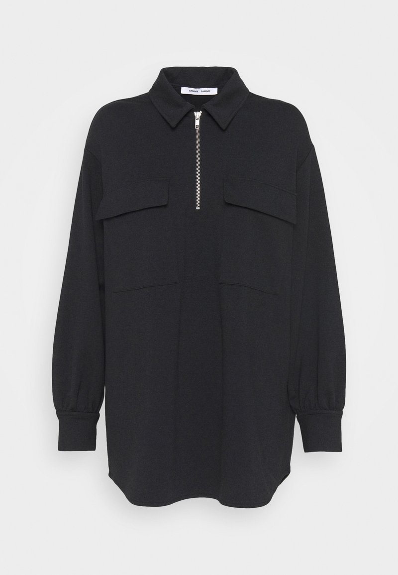 Chemise noire à manches longues avec un col zippé, deux poches avant et des manches bouffantes. Confectionnée dans un tissu doux avec une coupe décontractée.
