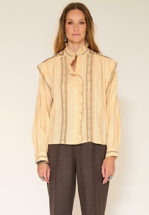 Blouse bouton de couleur jaune clair avec un col et des poignets à volants. Présente des rayures verticales et une broderie brune complexe le long du centre.