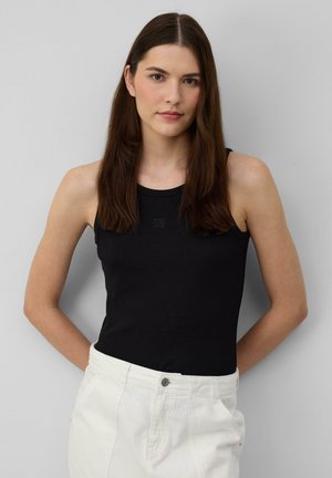 Top a maniche sottili in raso nero con scollatura rotonda, abbinato a pantaloni bianchi a vita alta con bottone visibile e dettagli delle tasche.