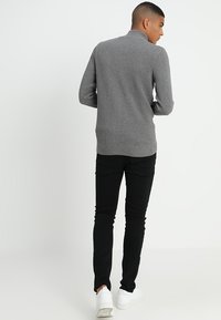 Grå strikkegenser med høy krage, høydepassende design, teksturert mønster, kombinert med svarte slim-fit bukser og hvite joggesko.