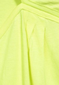 Neon žlutá látka s hladkým povrchem, s plisováním a prošitými švy. Design má soudržný, lehký vzhled.