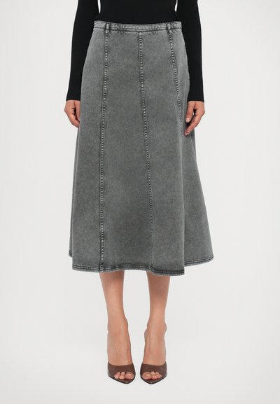 Grauer Midi-Jeansrock mit sichtbaren Nähten, getragen mit einem schwarzen Langarmoberteil und braunen offenen High Heels.