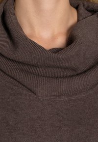 Sweter z kapturem wykonany z miękkiej, brązowej dzianiny o prążkowanej strukturze. Charakteryzuje się teksturowanym materiałem, luźnym krojem oraz brakiem widocznych elementów metalowych i wzorów.