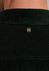 Donkergroene corduroy overhemdkraag met verticale ribbeling, voorzien van een klein rond "PME Legend" label nabij de halsnaad.