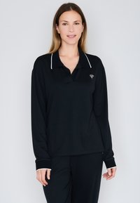 Černé polo tričko s dlouhým rukávem a bílými akcenty na límci a manžetách. Obsahuje malé logo na hrudi a má volný střih.
