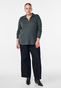 Dugulja s dugim rukavima, tamno siva pletiva s ovratnikom, u kombinaciji sa širokim tamnim trapericama i crnim čizmama s visokom potpeticom.