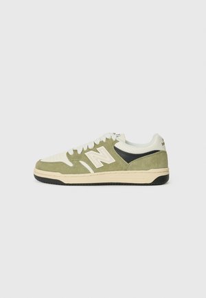 Baskets basses avec maille blanche, empiècements en daim vert, détail noir près du talon, lacets blancs et semelle beige sur fond uni.
