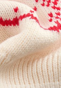Tissu tricoté crème mettant en valeur un motif géométrique rouge. La texture est douce et pelucheuse, avec des sections côtelées et lisses bien distinctes.