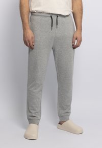 Graue Baumwoll-Sweatpants mit elastischem Bund, Kordelzug, zwei Seitentaschen und gerippten Bündchen. Kombiniert mit beigen Slippern.