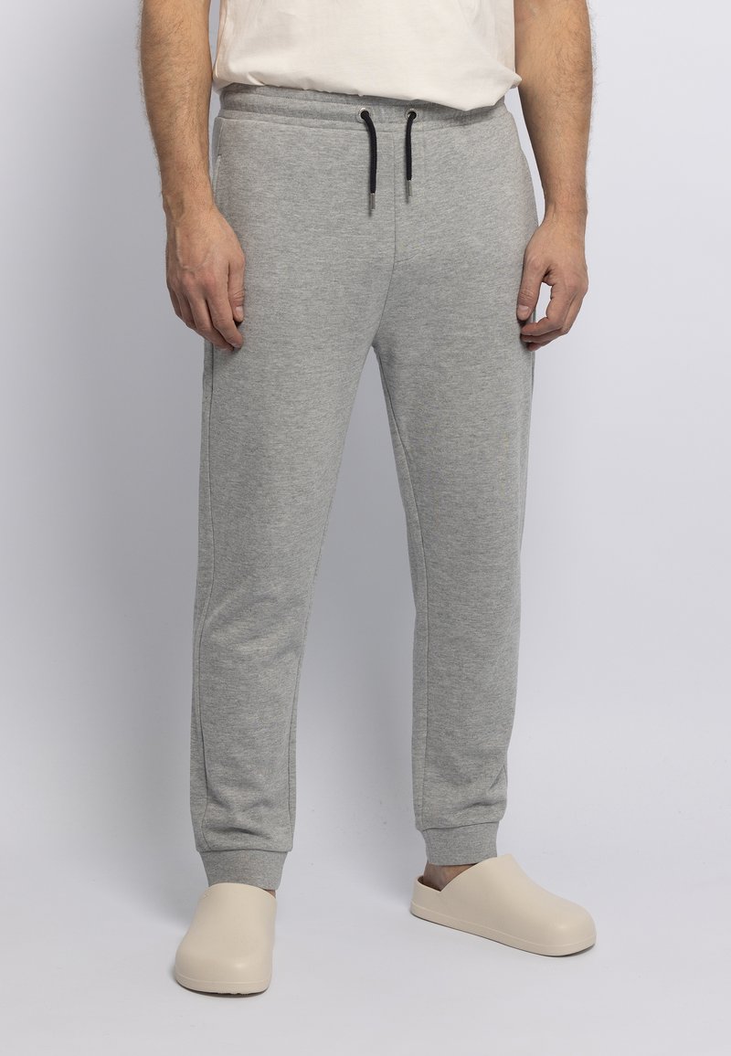Graue Baumwoll-Sweatpants mit elastischem Bund, Kordelzug, zwei Seitentaschen und gerippten Bündchen. Kombiniert mit beigen Slippern.