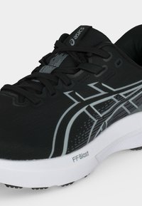 Μαύρο και γκρι παπούτσι τρεξίματος Asics με λευκή σόλα με την ένδειξη FF Blast, με κορδόνια και λογότυπο της μάρκας στο πλάι και στη γλώσσα.
