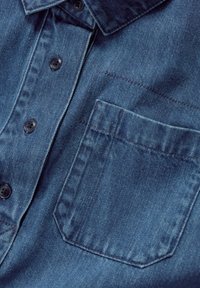 Dunkelblaue Jeanshemd mit spitzem Kragen, sechs schwarzen Knöpfen und einer einzelnen Brusttasche. Der Stoff zeigt eine klassische Textur.