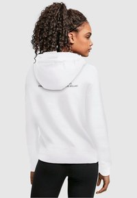 Hvid hoodie med kengurutaske og snorer til hætten. Tekst trykt på ryggen. Blødt stof og ribbede manchetter og kant.