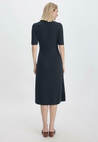 Knie-langes, dunkelgraues Strickkleid mit kurzen Ärmeln, gerippter Textur und leicht taillierter A-Linie. Offener Rücken mit dezentem Kragen-Detail.