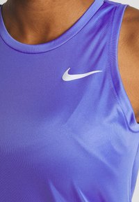 Débardeur de sport violet avec une texture lisse et brillante. Porte un logo Nike blanc sur la poitrine et un col rond classique.