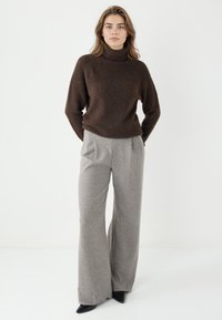 Brauner Rollkragenpullover mit einer weichen Textur, kombiniert mit hellgrauen, weit geschnittenen Hosen und schwarzen spitzen Pumps. Einfaches, modernes Design.