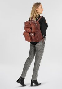 Zaino in pelle marrone con molteplici tasche frontali, spallacci regolabili e chiusura con zip. Texture liscia e design resistente.